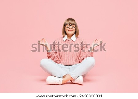 Full body elderly woman 50s years old wear sweater shirt casual clothes glasses sits hold hands in yoga om aum gesture relax meditate try calm down isolated on plain pink background. Lifestyle concept