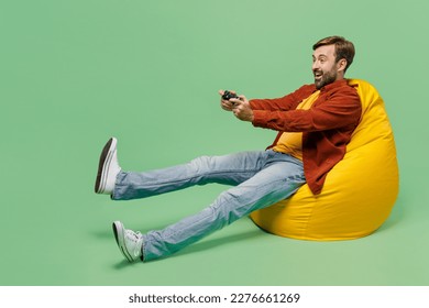 Full body excited elderly man 40s years old he wears casual clothes red shirt t-shirt sit in bag chair hold in hand play pc game with joystick console isolated on plain pastel light green background - Powered by Shutterstock