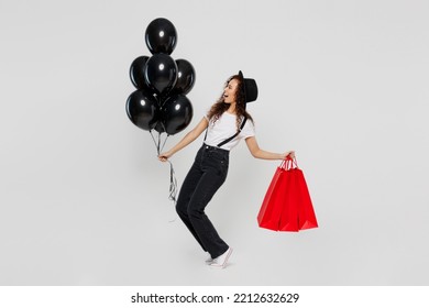 Full Body Excited Happy Young Woman Wear T-shirt Hat Hold In Hand Red Paper Package Bags After Shopping Bunch Of Balloons Isolated On Plain Solid White Background. Black Friday Sale Buy Day Concept