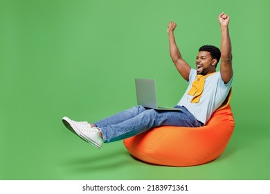 Full body excited young man of African American ethnicity 20s in blue t-shirt sit in bag chair hold use work on laptop pc computer do winner gesture isolated on plain green background studio portrait. - Powered by Shutterstock