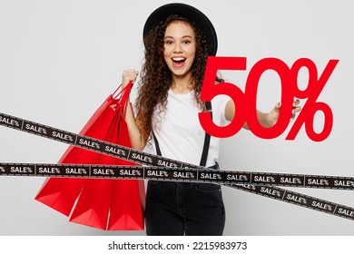 Full Body Excited Young Woman Wear T-shirt Hat Hold In Hand Red Paper Package Bags After Shopping Give 50 Percent Sale Sign Isolated On Plain Solid White Background. Black Friday Sale Buy Day Concept