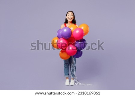 Full body excited young woman of Asian ethnicity she wear casual clothes red tank shirt hold bunch of colorful air balloons isolated on plain pastel light purple background studio. Lifestyle concept