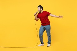 Full Body Expressive Singer Young Happy Indian Man He Wearing Red T-shirt Casual Clothes Sing Song In Microphone At Karaoke Club Isolated On Plain Yellow Orange Background Studio. Lifestyle Concept