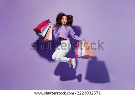 Full body exultant excited happy young woman wear pullover hold in hand paper package bags after shopping jump high isolated on plain pastel light purple background. Black Friday sale buy day concept