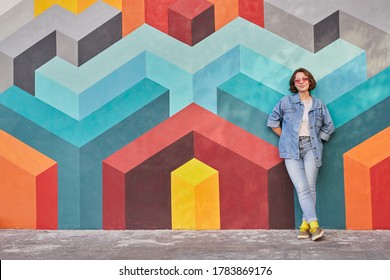 Full body female hipster in denim clothes leaning on colorful wall with geometric graffiti while resting on city street - Shutterstock ID 1783869176