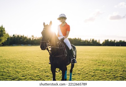 Full Body Of Female Polo Player With Reins In Hand Wearing Boots White Pants And Helmet With Face Guard Riding Bay Horse With Bridle And Wrapped Legs During Training On Playing Field