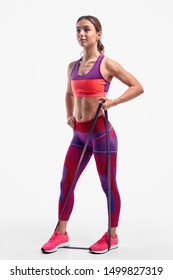 Full Body Fit Young Lady In Sportswear Pulling Elastic Band And Looking Away While Exercising Against White Background