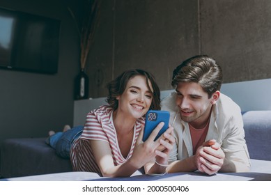 Full body front view young couple two friends woman man in casual clothes wired earphones lying sofa using mobile cell phone listen to music rest indoors at home flat together People lifestyle concept - Powered by Shutterstock