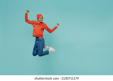 Full body fun cool young smiling happy african american man 20s in orange shirt hat do winner gesture jump high isolated on plain pastel light blue background studio portrait. People lifestyle concept