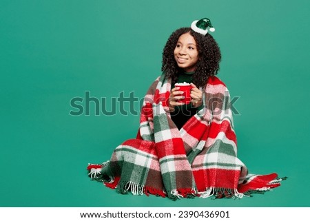 Full body fun merry little kid teen girl wrapped in plaid wear hat posing drink tea look aside isolated on plain green background studio portrait. Happy New Year celebration Christmas holiday concept