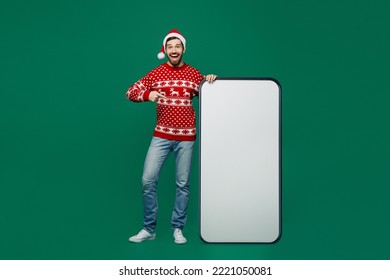 Full body fun merry young man wear red knitted sweater Santa hat posing point on big huge blank screen mobile cell phone with area isolated on plain dark green background New Year 2023 holiday concept - Powered by Shutterstock