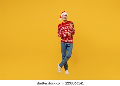 Full body fun merry young man wear red knitted Christmas sweater Santa hat posing hold takeaway delivery paper cup coffee to go isolated on plain yellow background. Happy New Year 2023 holiday concept - Powered by Shutterstock