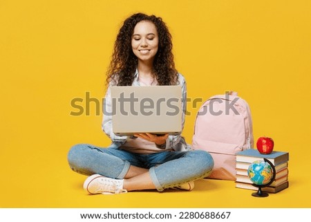 Full body fun young black teen girl student she wear casual clothes backpack bag hold use work on laptop pc computer isolated on plain yellow color background. High school university college concept