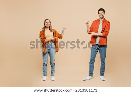 Full body fun young couple two friends family man woman wear casual clothes together point index finger between them on workspace area mock up isolated on pastel plain beige color background studio