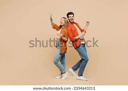 Full body fun young couple two friends family man woman wear casual clothes point index finger aside on area waving hand together isolated on pastel plain light beige color background studio portrait