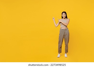Full body fun young latin woman 30s she wear basic beige tank shirt point index finger aside indicate on workspace area copy space mock up isolated on plain yellow backround. People lifestyle concept