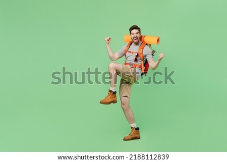 Full body fun young traveler white man carry backpack stuff mat walk do winner gesture isolated on plain green background. Tourist leads active healthy lifestyle. Hiking trek rest travel trip concept