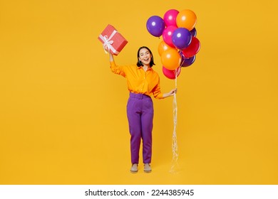 Full body fun young woman wear casual clothes hat celebrating hold bunch of balloons raise up present box with gift ribbon bow isolated on plain yellow background. Birthday 8 14 holiday party concept - Powered by Shutterstock