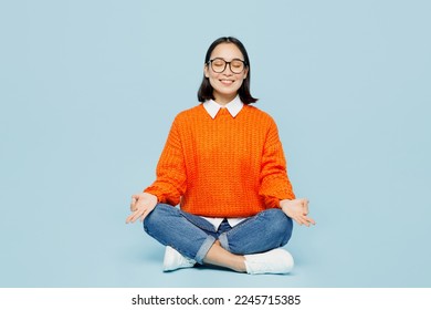 Full body fun young woman of Asian ethnicity wear orange sweater glasses hold spreading hands in yoga om aum gesture relax meditate try to calm down isolated on plain pastel light blue cyan background - Powered by Shutterstock