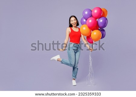 Full body funny young woman of Asian ethnicity she wears casual clothes red tank shirt hold bunch of colorful air balloons isolated on plain pastel light purple background studio. Lifestyle concept