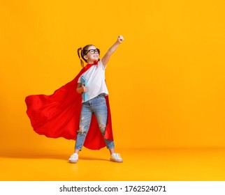 Full body girl in superhero cape smiling and raising fist up while being ready for school studies against yellow backdrop