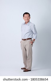 Full Body Of An Happy Asian Old Man In Light Grey Shirt And Beige Pants Standing In Studio White Background.