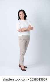 Full Body Of An Happy Asian Old Woman In White Shirt And Beige Pants Standing In Studio White Background.