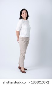 Full Body Of An Happy Asian Old Woman In White Shirt And Beige Pants Standing In Studio White Background.