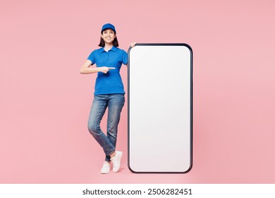 Full body happy delivery employee woman wear blue cap t-shirt uniform workwear work as dealer courier point index finger on big huge blank screen mobile cell phone isolated on plain pink background - Powered by Shutterstock