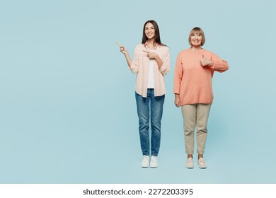 Full body happy elder parent mom with young adult daughter two women together wear casual clothes point index finger aside on area show thumb up isolated on plain blue background. Family day concept - Shutterstock ID 2272203395