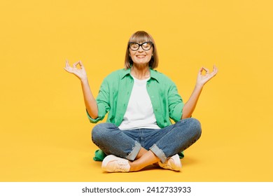 Full body happy elderly woman 50s years old wear green shirt glasses casual clothes sitting hold spread hands in yoga om aum gesture relax meditate try calm down isolated on plain yellow background - Powered by Shutterstock