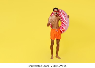 Full body happy fun young man wear orange shorts swimsuit relax near hotel pool hold pink donut rubber ring show thumb up isolated on plain yellow background Summer vacation sea rest sun tan concept - Powered by Shutterstock