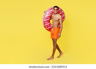 Full body happy fun young man wear orange shorts swimsuit relax near hotel pool hold pink donut rubber ring walking going isolated on plain yellow background Summer vacation sea rest sun tan concept - Powered by Shutterstock