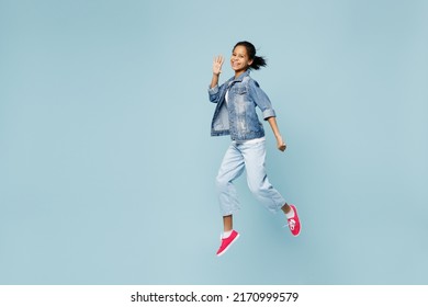 Full body happy little kid teen girl of African American ethnicity 12-13 years old in denim jacket jump high waving hand look camera isolated on pastel plain light blue background. Childhood concept - Shutterstock ID 2170999579