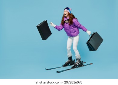 Full Body Happy Skier Woman In Warm Purple Padded Windbreaker Jacket Ski Goggles Mask Spend Weekend In Mountains Holding Package Bags With Purchases Shopping Isolated On Plain Blue Background Studio