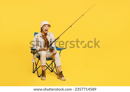 Full body happy surprised shocked young woman sitting holding fishing rod isolated on plain yellow background. Tourist leads active lifestyle walk on spare time. Hiking trek rest travel trip concept