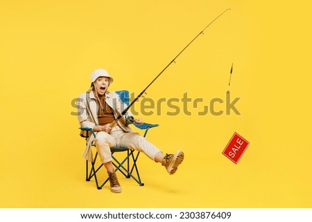 Full body happy surprised young woman sit hold fishing rod with sale text isolated on plain yellow background. Tourist leads active lifestyle walk on spare time. Hiking trek rest travel trip concept