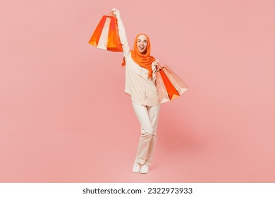 Full body happy young arabian asian muslim woman wearing orange abaya hijab hold shopping package bags isolated on plain pink background. Black Friday sale buy day, uae middle eastern islam concept - Powered by Shutterstock