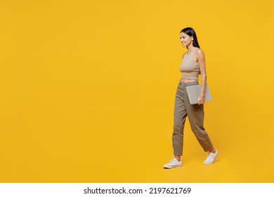 Full Body Happy Young Latin Woman 30s She Wear Basic Beige Tank Shirt Hold Closed Laptop Pc Computer Walking Going Stroling Isolated On Plain Yellow Backround Studio Portrait. People Lifestyle Concept