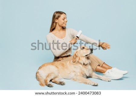 Full body happy young owner woman wear casual clothes cleaning shirt fur with roller sits near her best friend retriever dog isolated on plain light blue background studio. Take care about pet concept