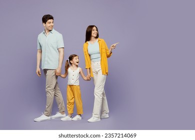 Full body happy young parents mom dad child kid daughter girl 6 years old wearing blue yellow casual clothes hold hands walk go point back aside isolated on plain purple background. Family day concept - Powered by Shutterstock