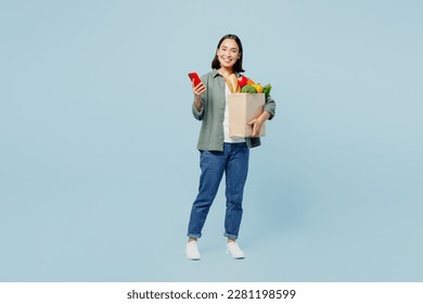 Full body happy young woman in casual clothes hold brown paper bag with food products use mobile cell phone isolated on plain blue background studio portrait. Delivery service from shop or restaurant - Powered by Shutterstock