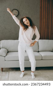 Full body happy young woman wear casual clothes stand near grey sofa couch dance raise up hands have fun stay at home hotel flat rest relax spend free spare time in living room indoor. Lounge concept - Shutterstock ID 2367234493