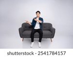 Full body image of young Asian man posing on sofa on white background