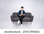 Full body image of young Asian man using phone sitting on sofa on white background