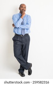 Full Body Indian Businessman Hand On Chin And Looking Up Having A Thought, Standing On Plain Background With Shadow 