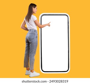 Full Body Length Back View Of Woman Using Big Smartphone With Blank White Screen And Touching Display Panel With Finger, Cheerful Lady Standing On Yellow Background, Ordering Food Delivery, Mock Up
