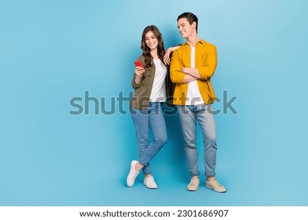 Full body length cadre of positive good mood couple choosing home decor website hold phone browsing ikea internet isolated on blue color background