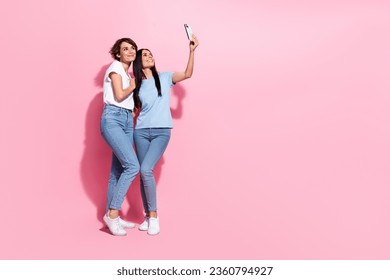Full body length cadre of two friendly charming girls sisters spend free time shopping mall selfie camera isolated on pink color background