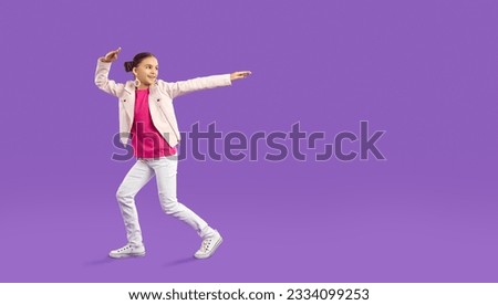 Full body length happy cheerful pretty little girl in pink T shirt, white leather jacket, jeans and trainers pointing at purple copy space background. Children's clothes, kid's fashion, sale concept